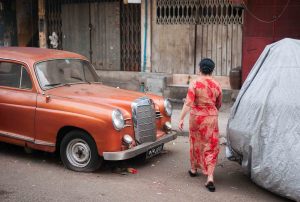 a woman with a dress walks past an old car in yangon burma. Street photography in Myanmar